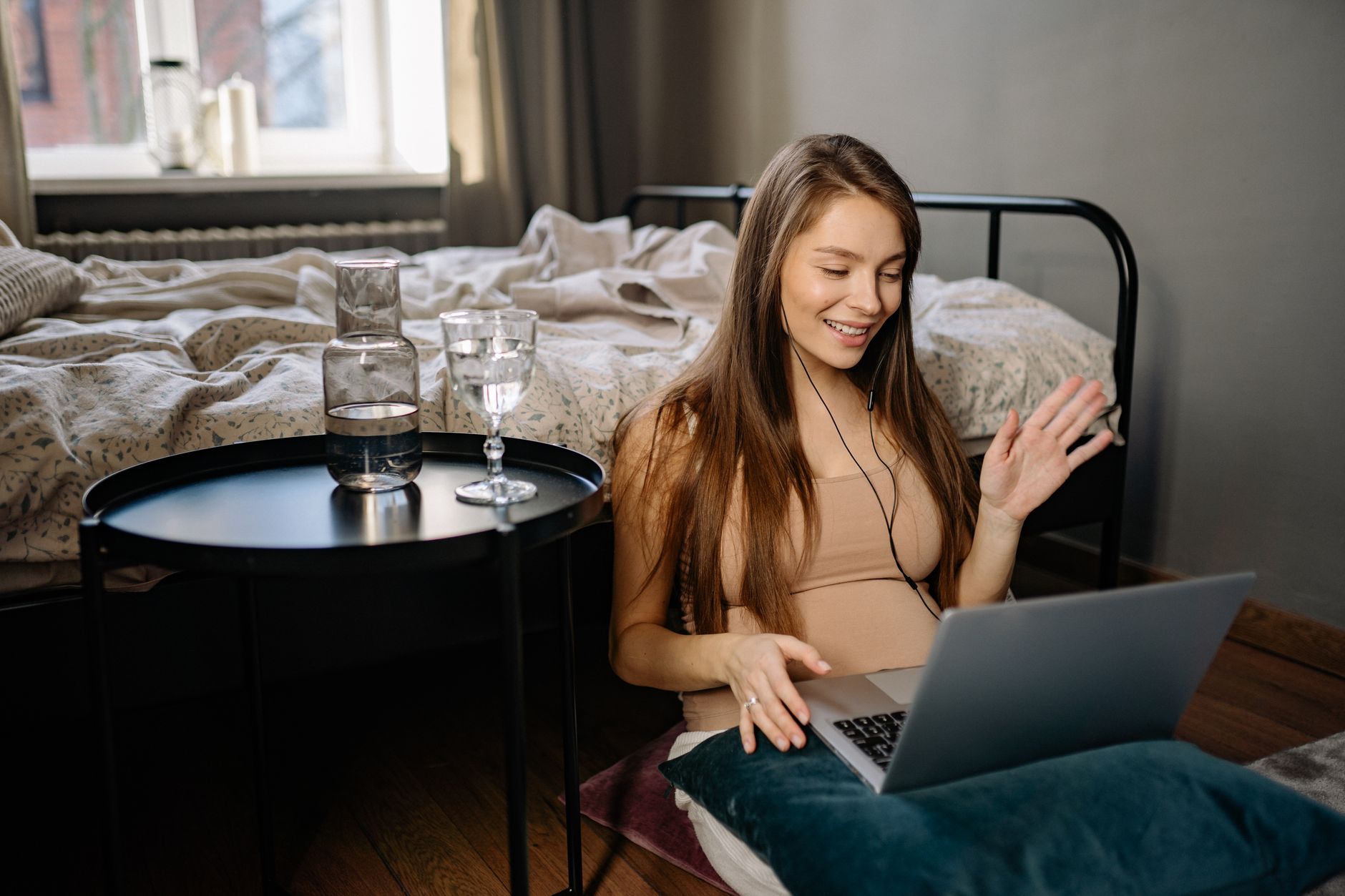 A woman waves at her laptop during a video call