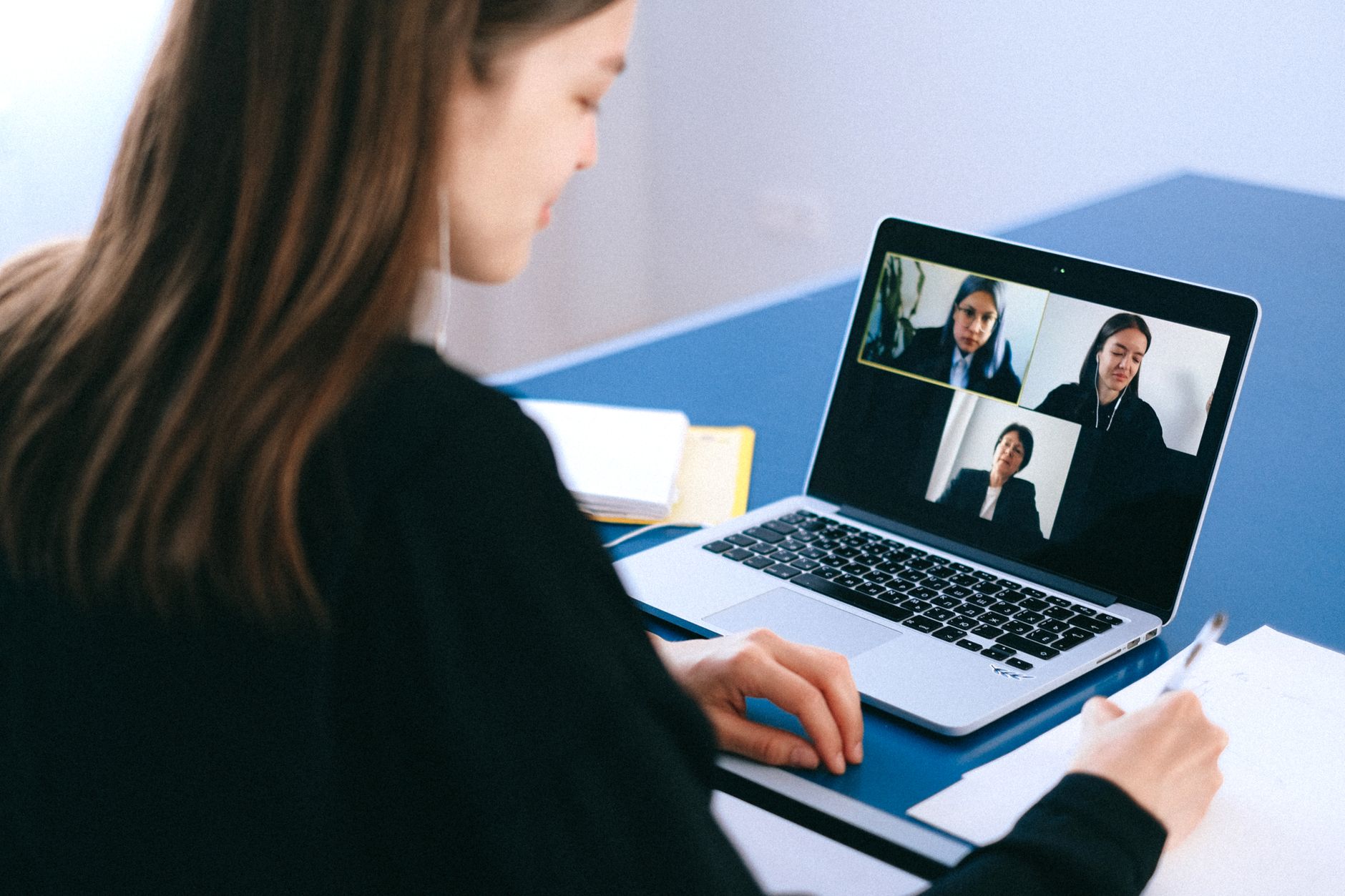 A woman takes notes during a video call with a grid of participants