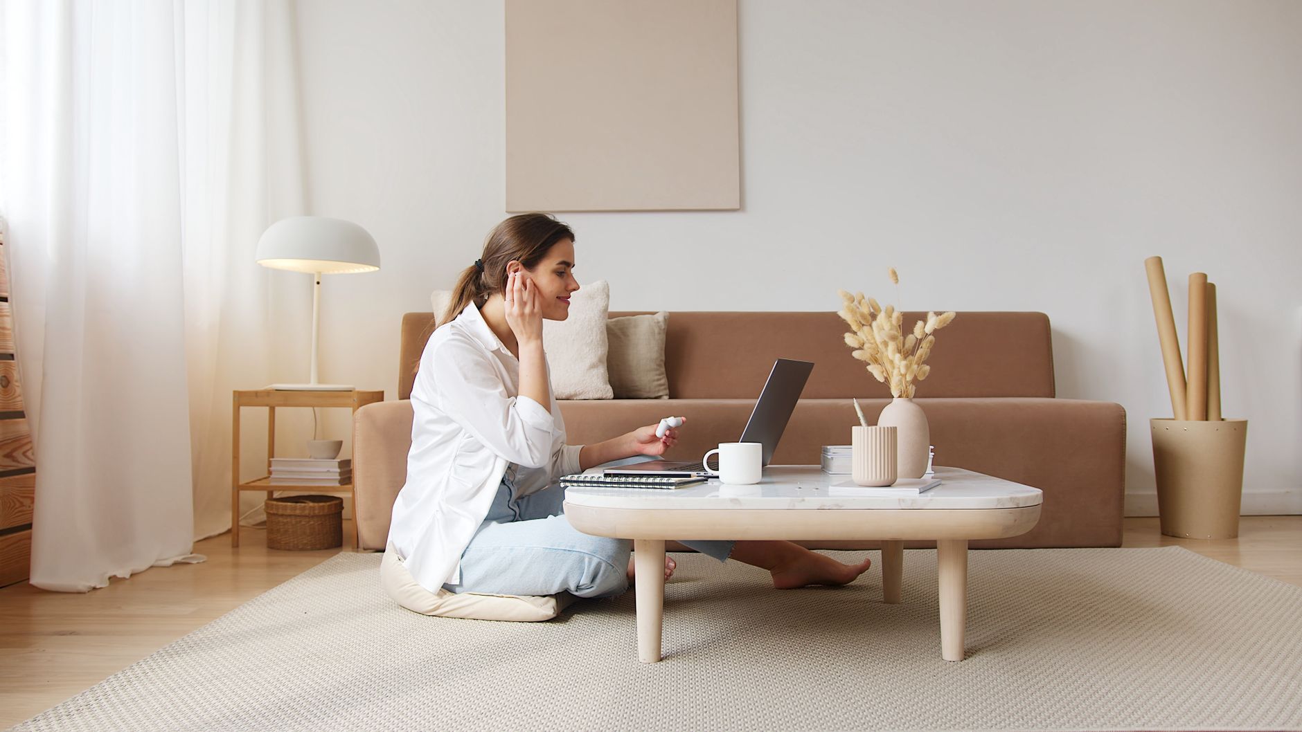 A woman with earbuds talks to a laptop from the living-room floor
